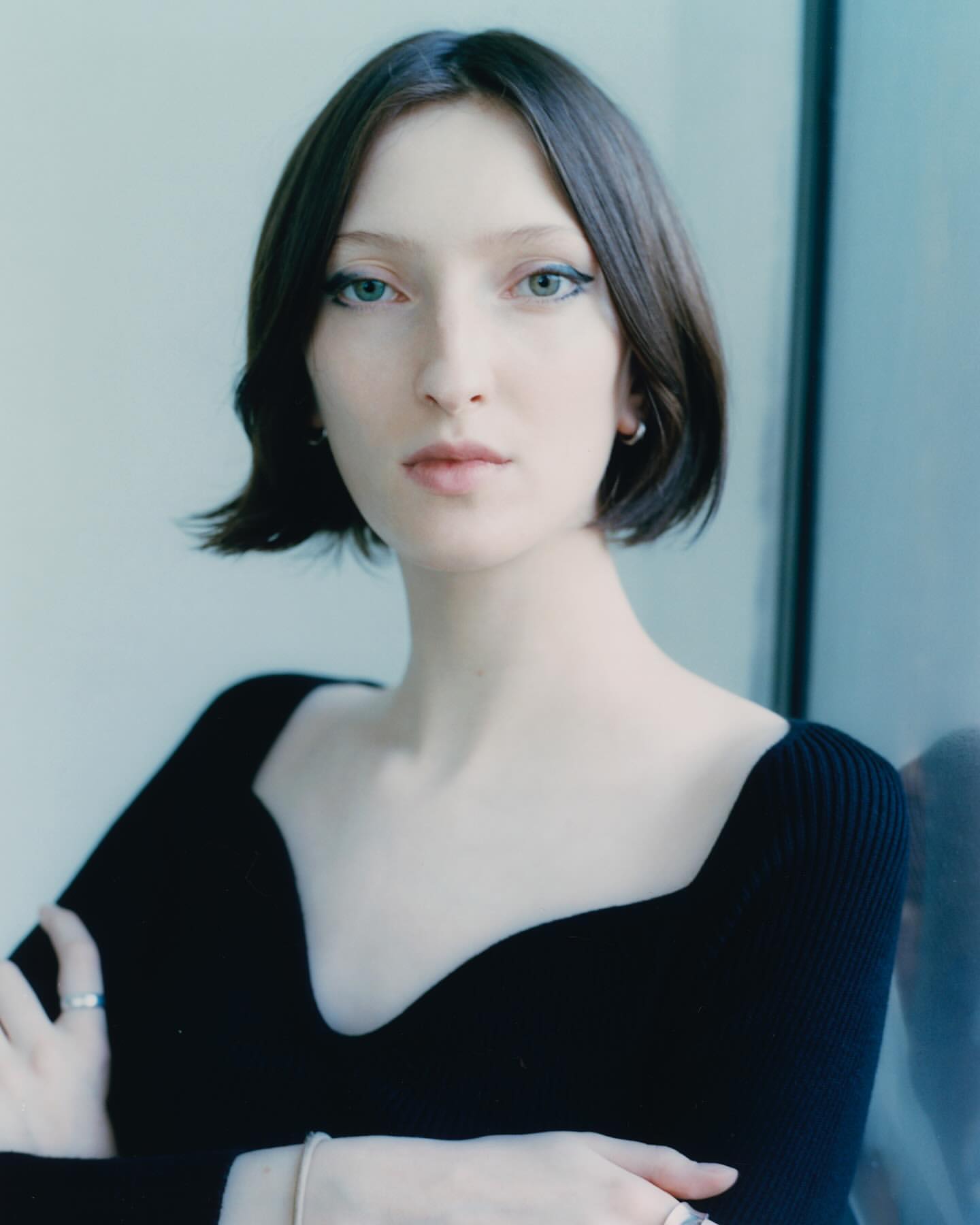 Portrait of a woman with short dark hair wearing a black top and silver rings against a plain background.