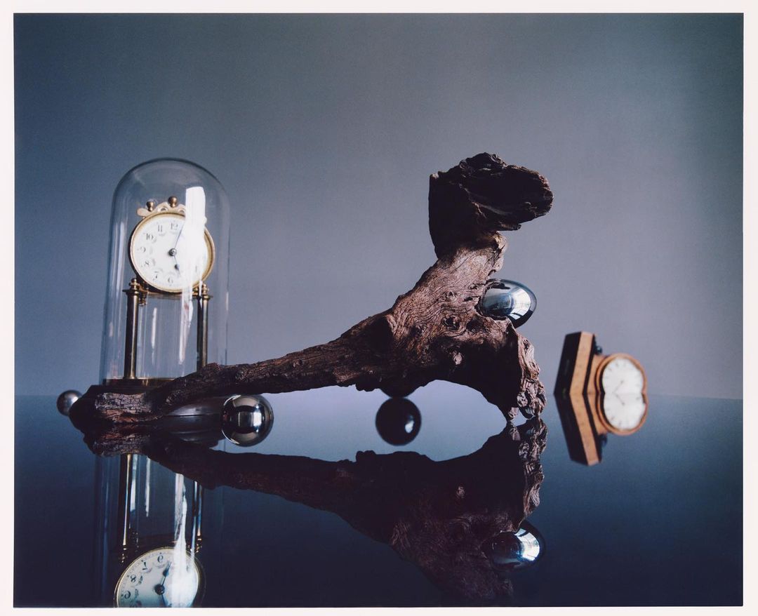 Still life with vintage clocks under glass domes, reflecting on a shiny surface with scattered chrome spheres. Contemporary art.