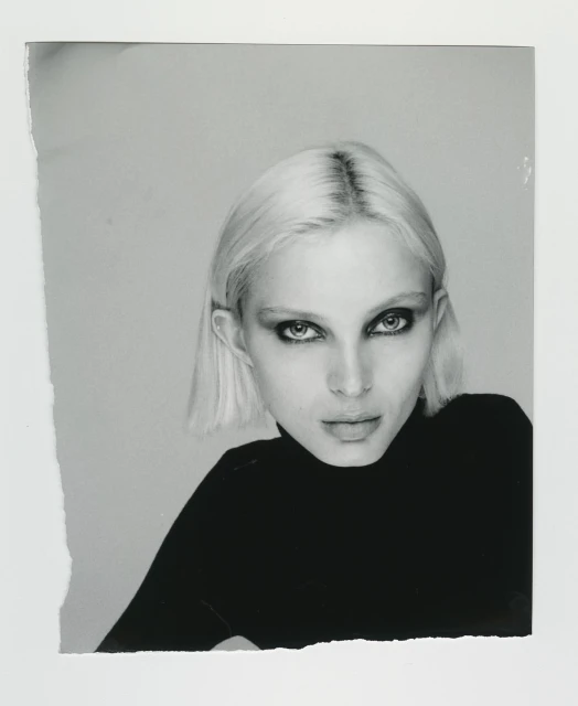 Monochrome close-up of a fair-skinned adult woman with short blonde hair, wearing a black top, and staring directly at the camera.