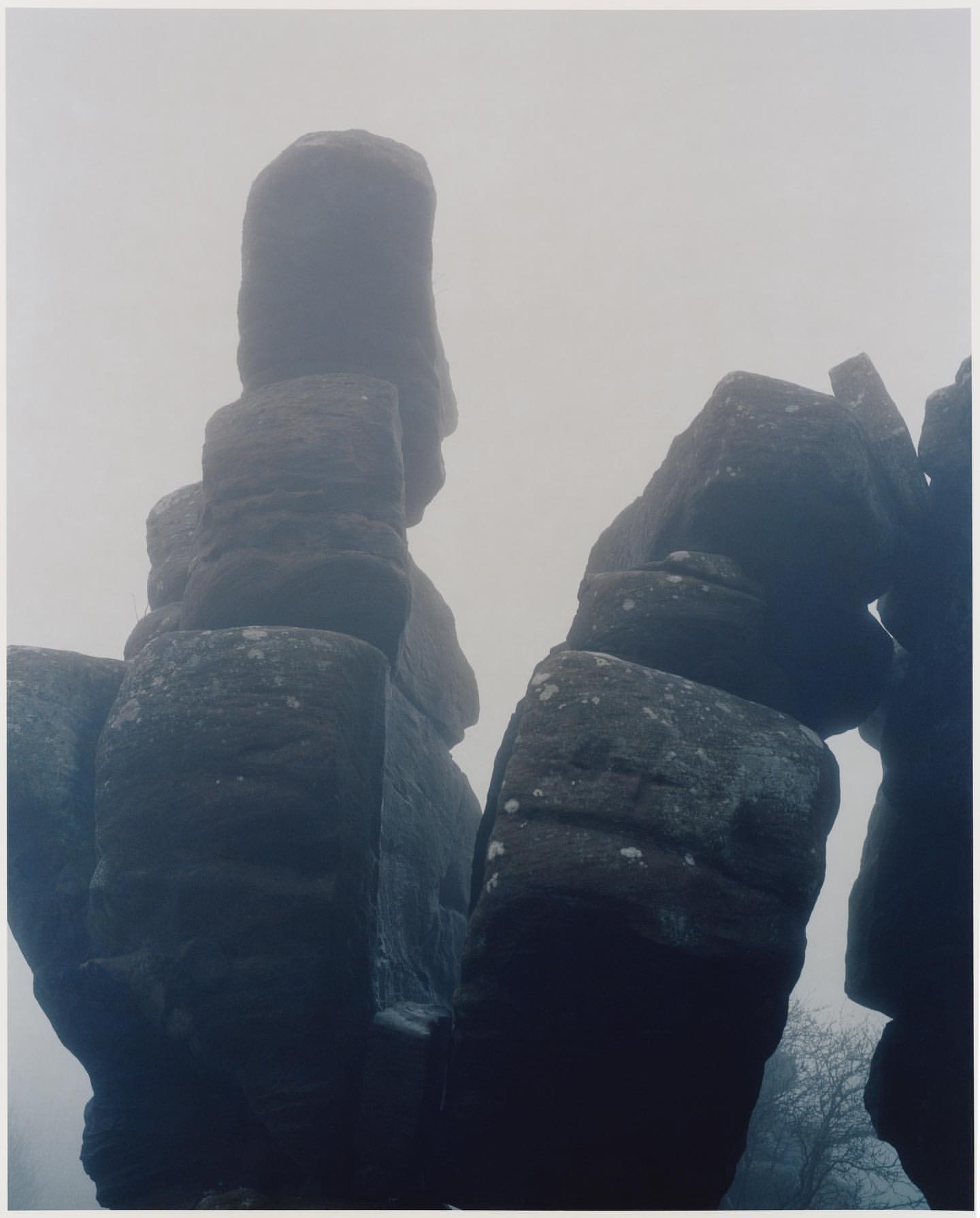 Dramatic rock formations rise through dense fog, creating a mysterious, imposing natural landscape with a muted color palette.