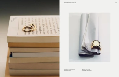 Editorial magazine spread featuring a gold ring resting on stacked books and a second gold ring placed on rolled paper.