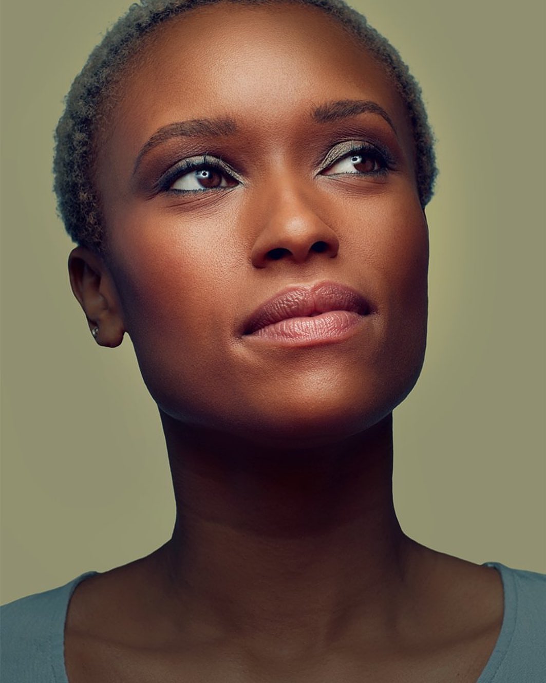 Portrait of an African American woman with short grey hair looking up and away from camera in a brightly lit studio setting.