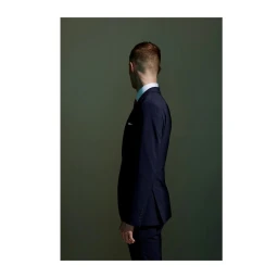 Profile of a man in a navy suit jacket and white shirt standing against a muted dark green background by photographer David Boni.