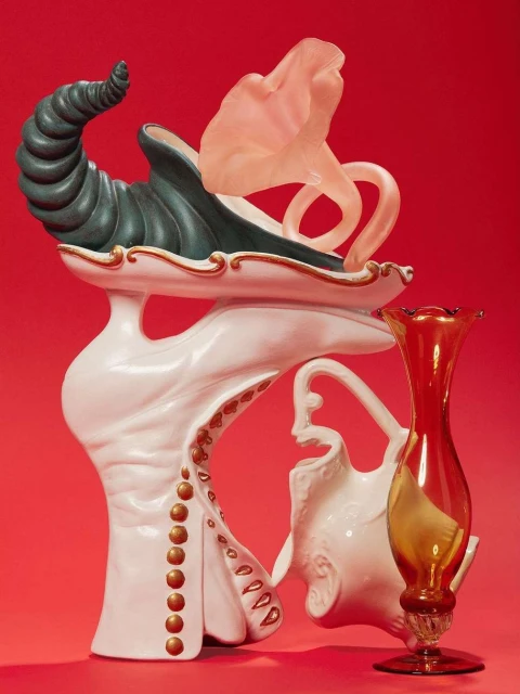 Still life photograph of sculptural vessels in various shapes and materials, placed against a red background in a studio setting.