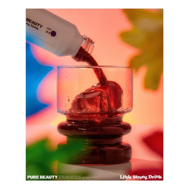 Close-up shot of red liquid being poured from a white bottle into a glass with ice cubes, set against a colorful, blurred background.