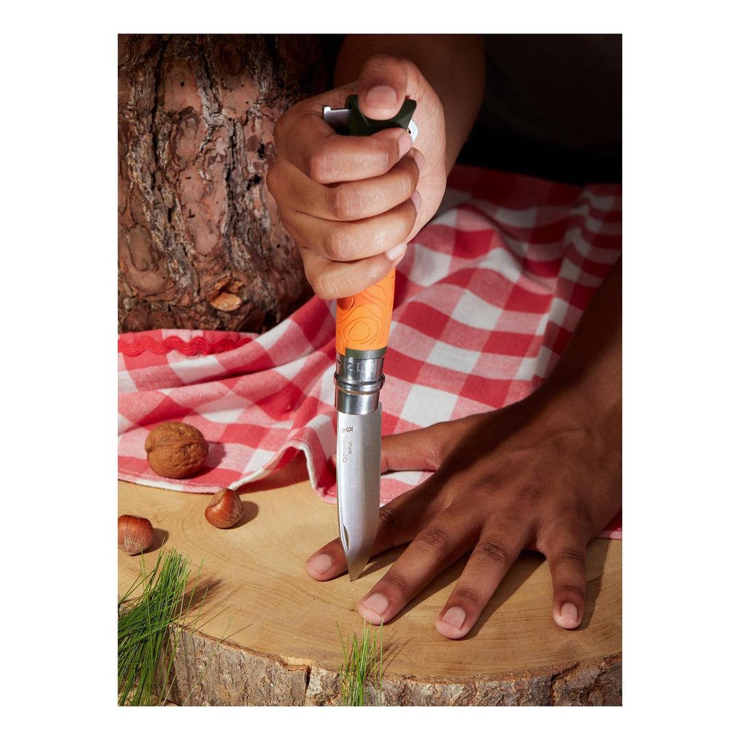 Person using a folding knife to stab a tree stump on top of a red and white checkered picnic blanket with walnuts nearby.