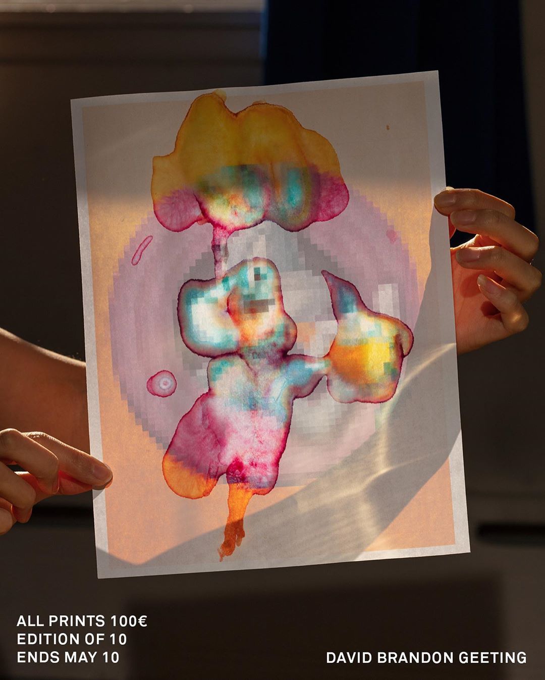 Abstract watercolor art print held up against natural light, featuring a blend of yellow, pink, and blue hues with visible texture.
