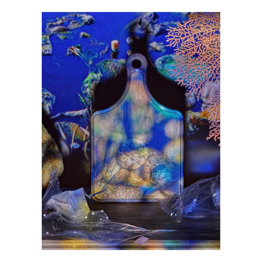Conceptual art with a cutting board featuring an underwater scene, plastic waste, and coral against a deep blue background with bokeh.