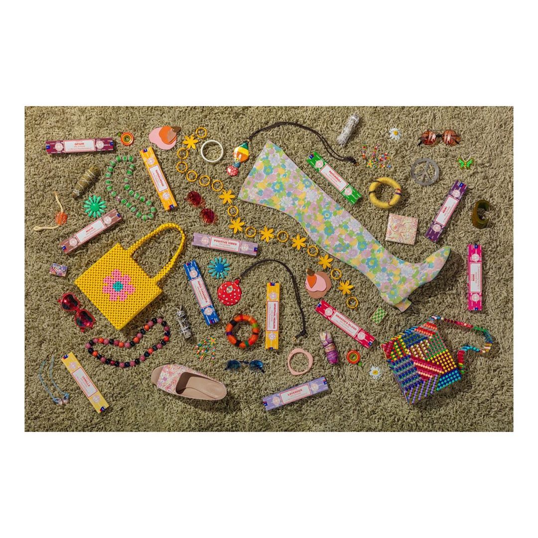 Flat lay of colorful accessories, beaded bags, floral tights, jewelry, sunglasses, and shoes arranged on a textured, olive green surface.