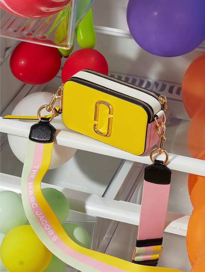 Yellow Marc Jacobs purse inside refrigerator with balloons in background, featuring a colorful strap, and gold hardware.