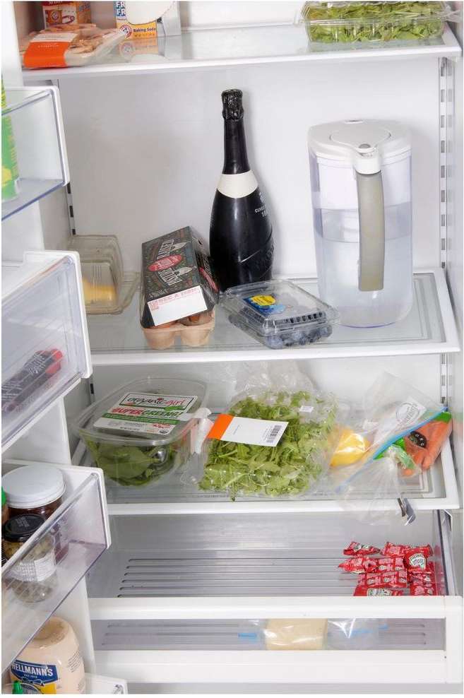 Inside of a refrigerator filled with food and drink items, including fruit, vegetables, eggs, sparkling wine, and a water filter pitcher.