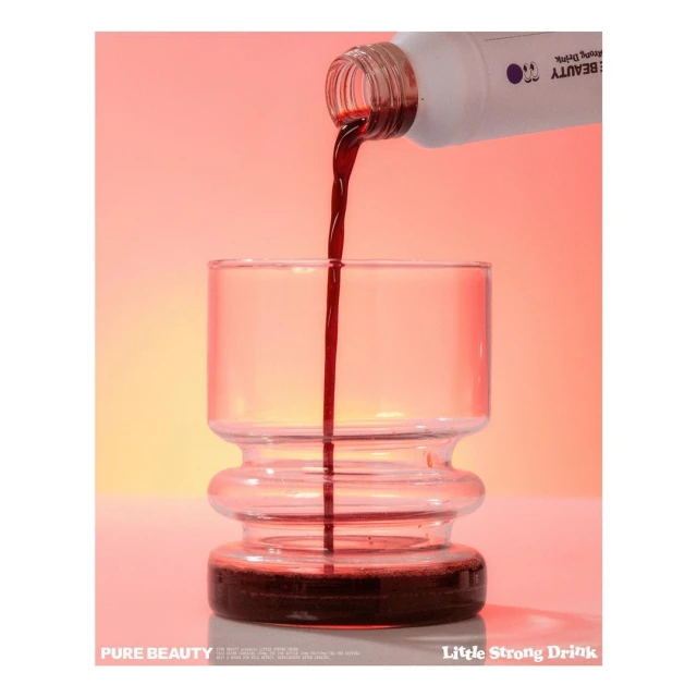 Pouring red beverage from a white bottle into an clear glass in front of a gradient peach and white background. Beverage concept.