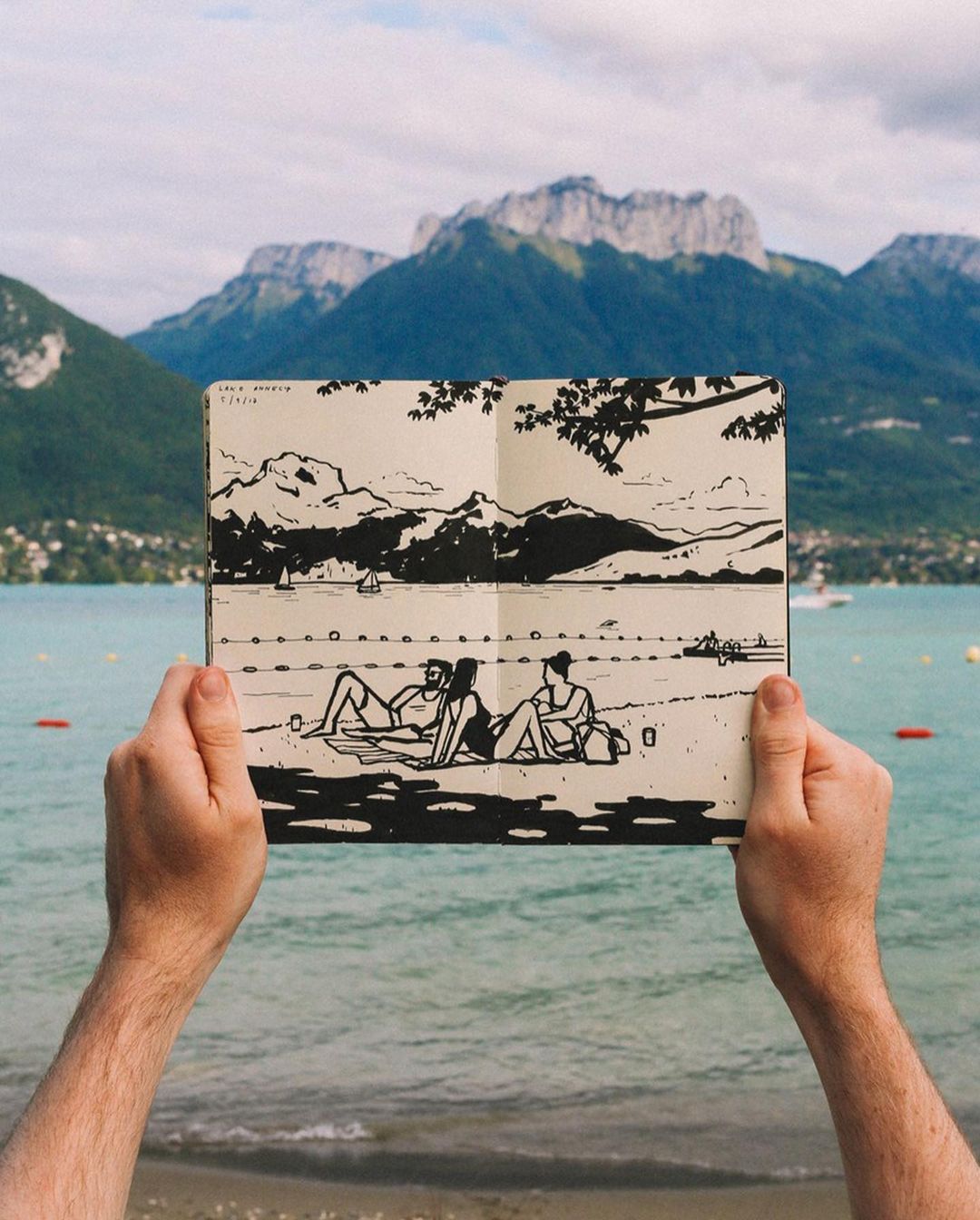 Handheld illustration of two figures on a beach, set against a backdrop of a lake, mountains, and a sky with scattered clouds.