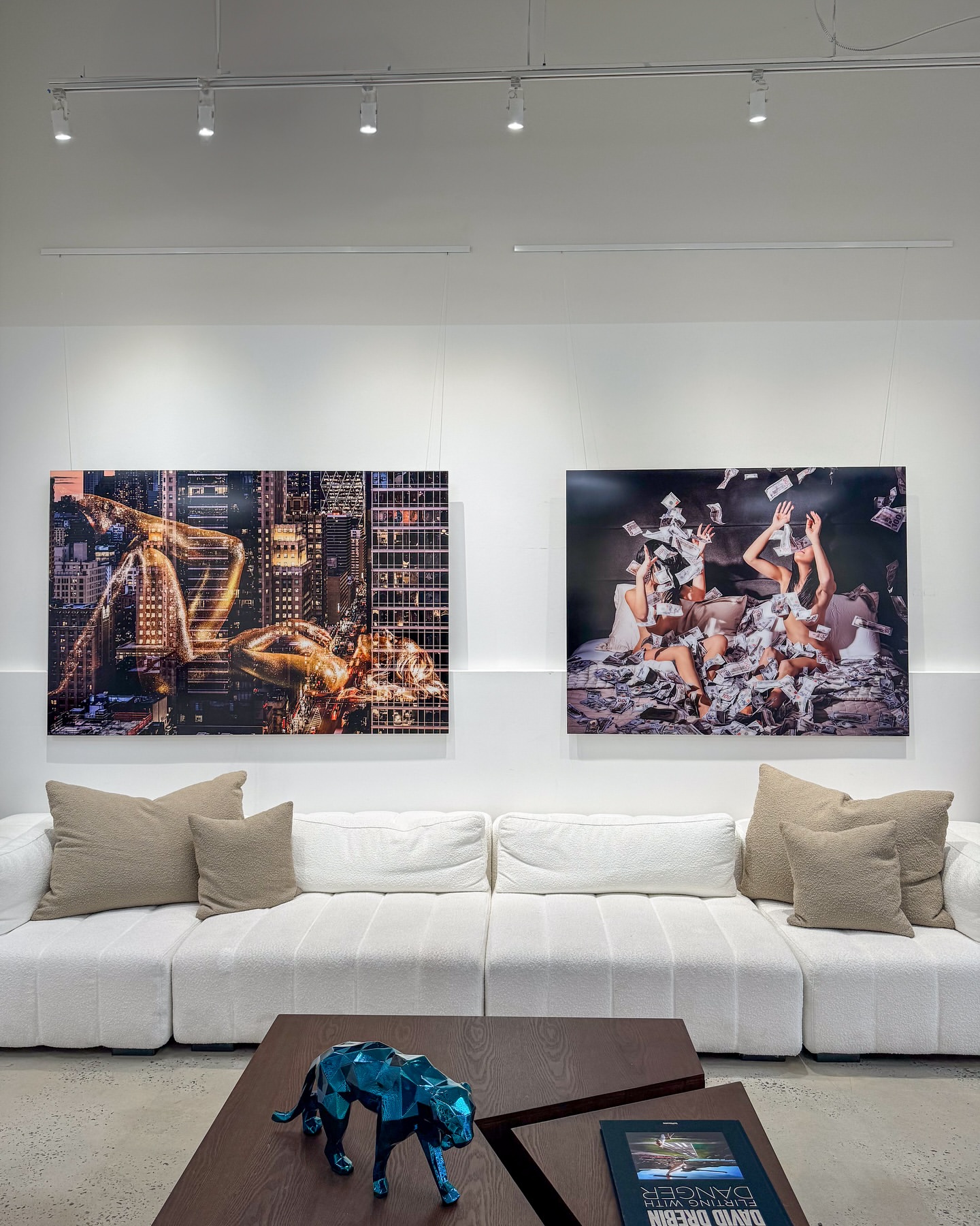 Interior view of modern white seating area featuring artwork of human figures against cityscapes and a decorative blue animal statue.