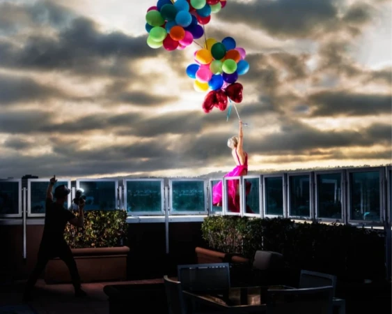 Woman in pink dress holding colorful balloons on rooftop with photographer