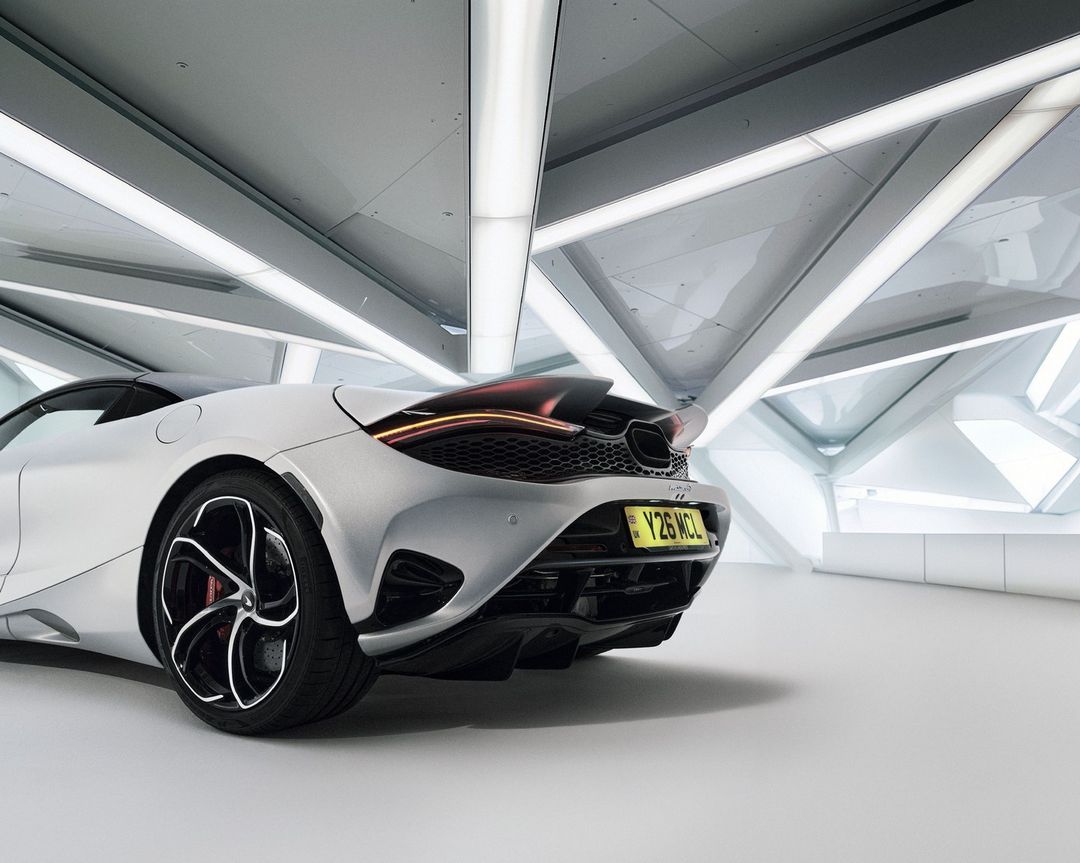 Silver McLaren sports car rear view in a modern showroom with geometric ceiling lights, showcasing automotive design and luxury.
