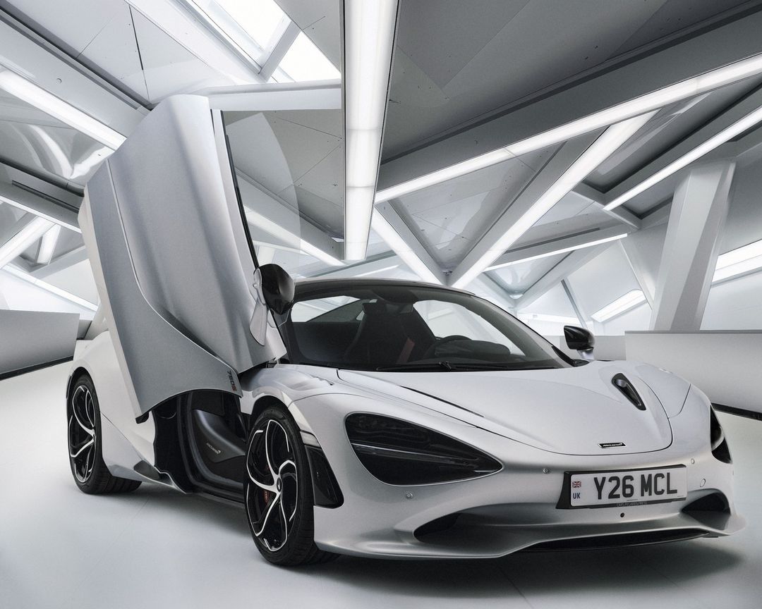 Silver McLaren sports car with open door in a showroom with geometric lighting reflecting off the glossy automotive paint.