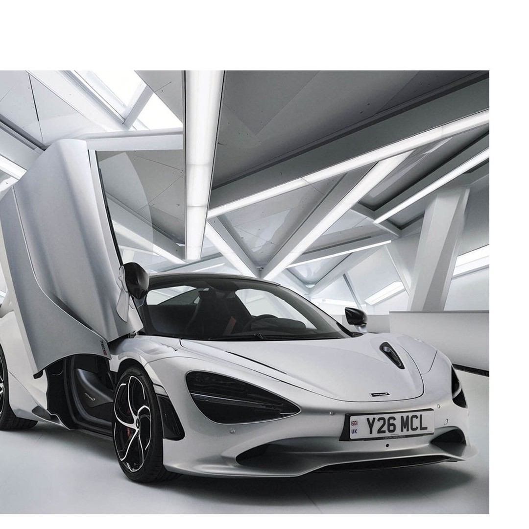 Silver Mclaren sports car with open doors, displayed in an indoor showroom with geometric architectural background lighting.