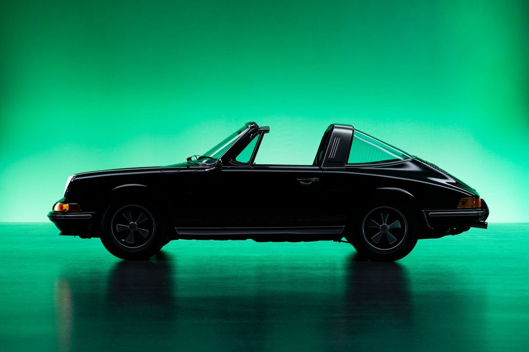 Side view of a classic black sports car with a Targa top against a vibrant green background, highlighting its sleek design.