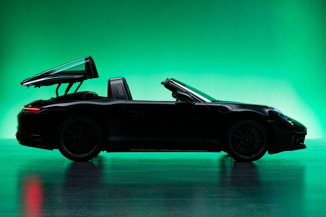 Profile view of a black Porsche Targa with its roof partially retracted against a gradated green background, conveying luxury and modern automotive design.