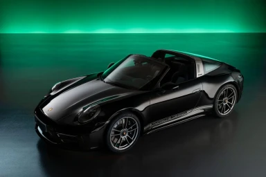 Sleek black Porsche convertible sports car parked in a studio with a vibrant green glowing horizon light on the wall.