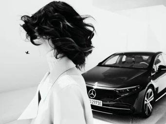Woman with dark wavy hair in profile wearing a coat with a black car parked in the background