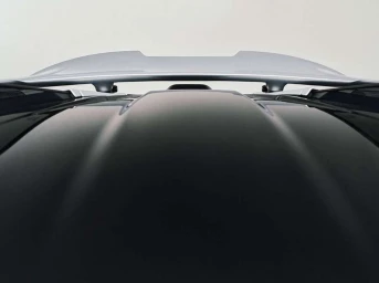 Close-up rear view of a dark luxury car roof featuring a prominent silver spoiler against a pale background