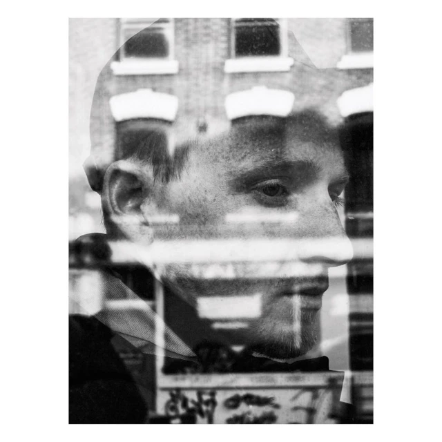 Monochrome portrait of a young man with a building reflection creating a double exposure effect, rendered in black and white with visible texture.