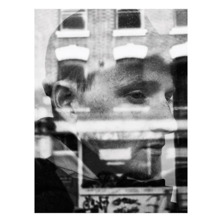 Monochrome portrait of a young man with a building reflection creating a double exposure effect, rendered in black and white with visible texture.