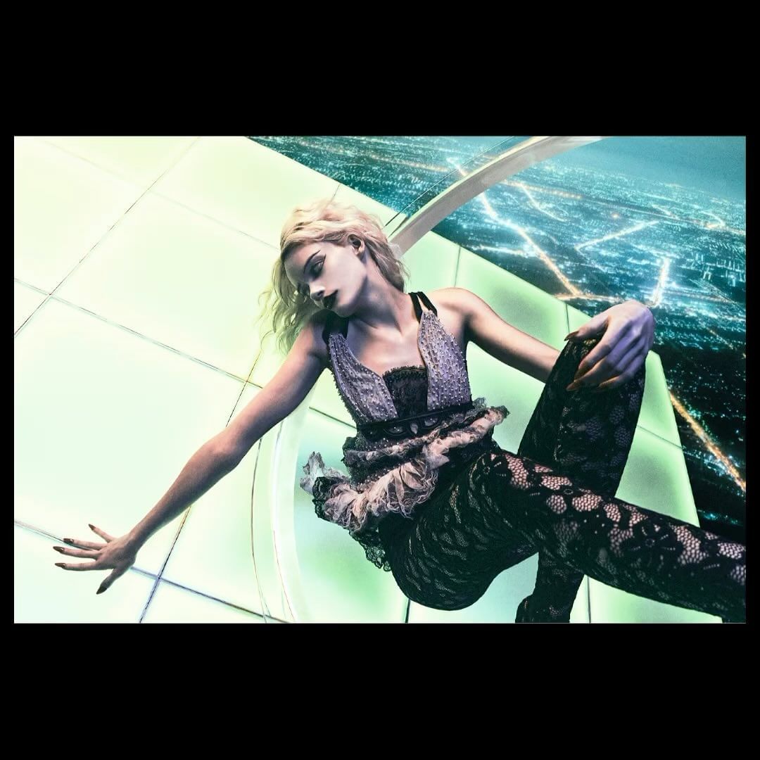 Fashion shot of a blonde adult female model in lace top and leggings, indoors with a city lights background, fashion studio photography.