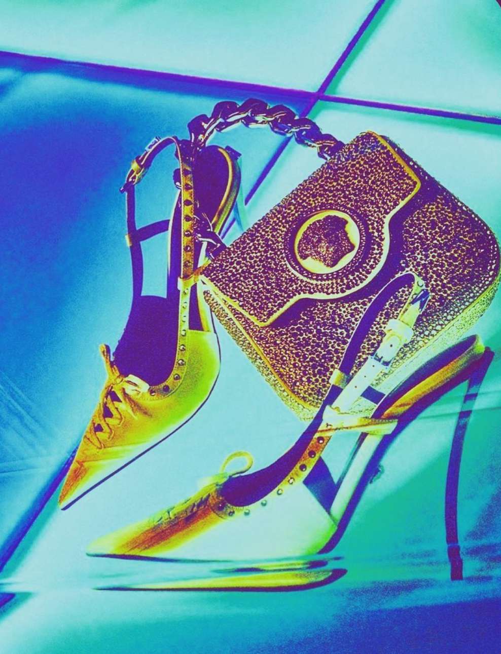 Elevated view of a gold colored purse and gold sling back high heeled shoes against a turquoise reflective surface.