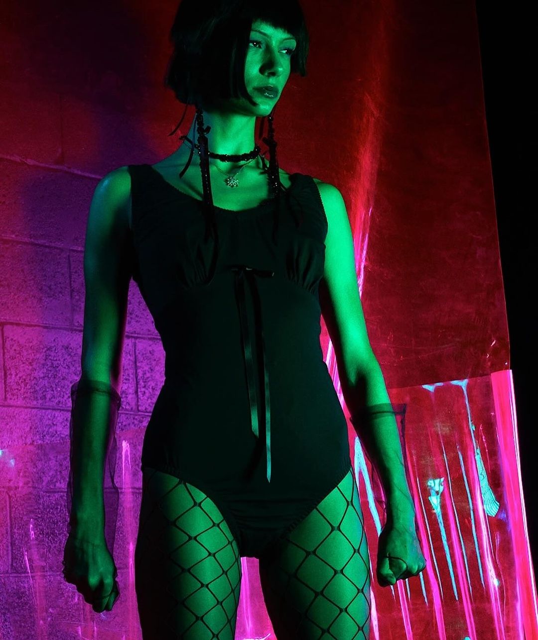 Model in black bodysuit and fishnet tights under green and pink dramatic lighting by David Hughes