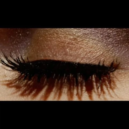 Close-up shot of a single closed eye with long, dark lashes and brown eyeshadow on fair skin. Beauty and makeup concept.