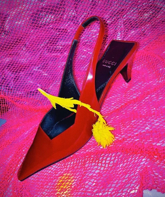 Red patent-leather slingback heel featuring a yellow flower against a bright pink textured background with the Gucci logo visible.