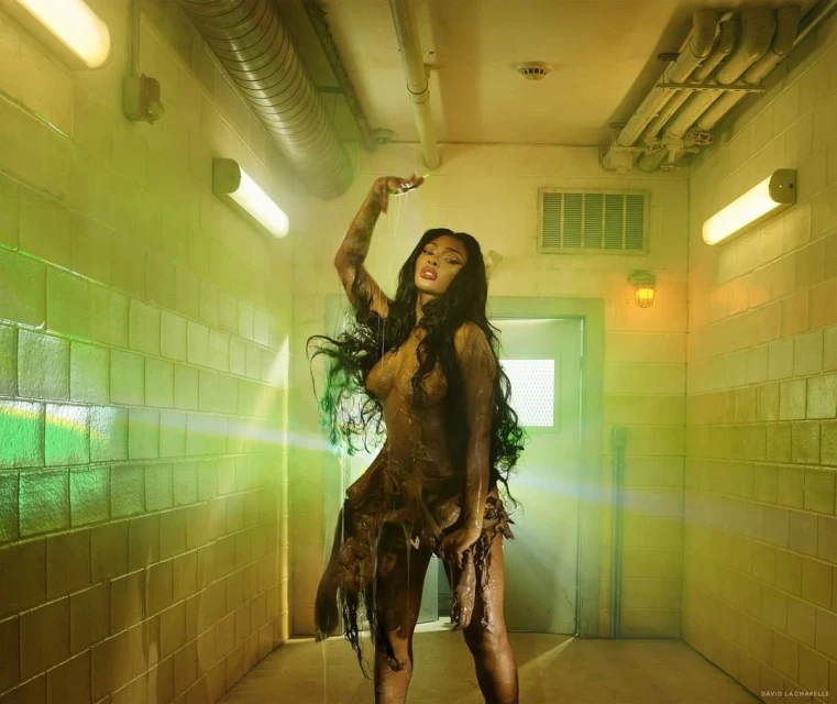 A dark-haired woman poses with water dripping on her in a tile-lined interior. Moody, low-key lighting, and earth-toned color palette.