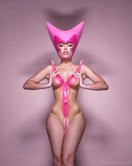 Adult female posing with creative pink headwear and bodysuit in a pink photo studio. Studio lighting and fashion forward design.