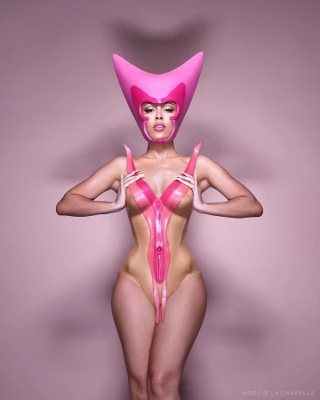 Woman wearing a pink latex bodysuit and horned headpiece against a matching pink studio backdrop
