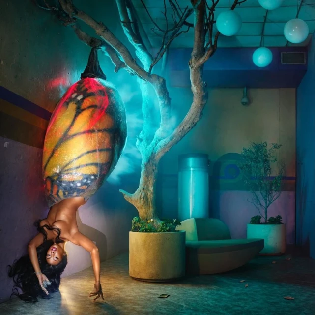Artistic portrait of a woman bending backwards beneath a butterfly wing-shaped lamp, with indoor plant and minimalist interior design.