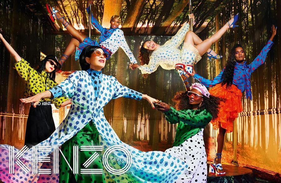 Fashion campaign featuring six diverse models in patterned outfits striking poses in front of a forest backdrop and the brand KENZO Paris.