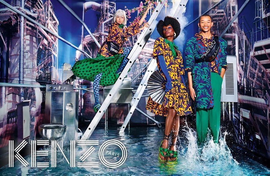 Fashion editorial shot featuring three diverse models in vibrant patterned outfits posing in an urban, water-filled setting for Kenzo Paris.