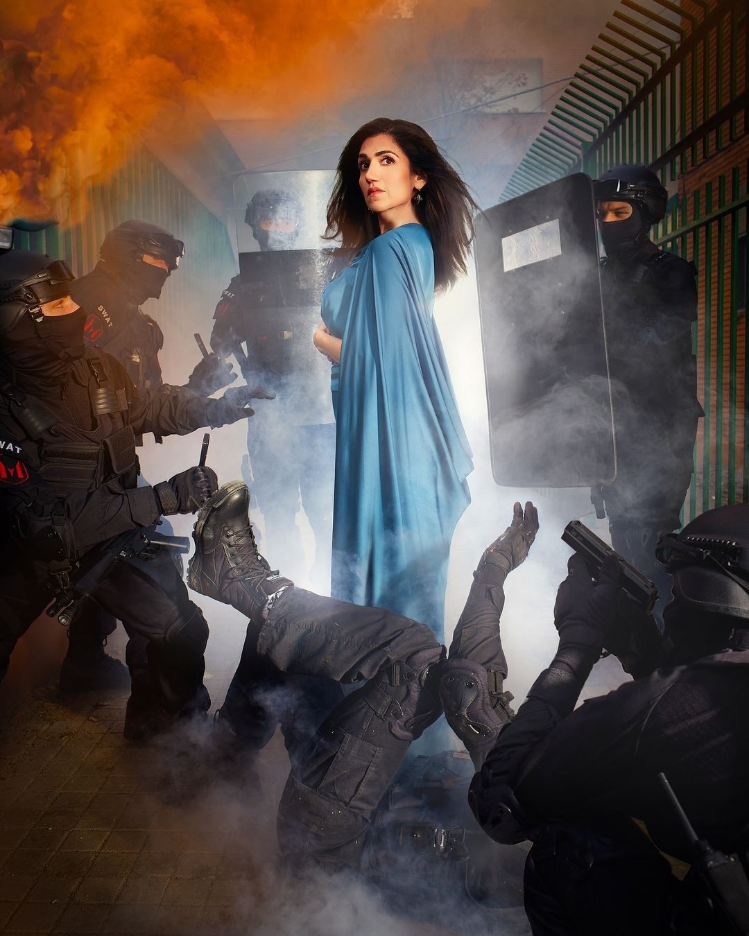 A woman in a blue dress stands among SWAT team members in riot gear, creating a striking and tense visual narrative.