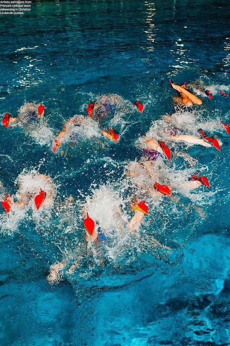 Synchronized swimming team in pool with red headpieces. A group of athletes performing in water, creating splashes in turquoise water.