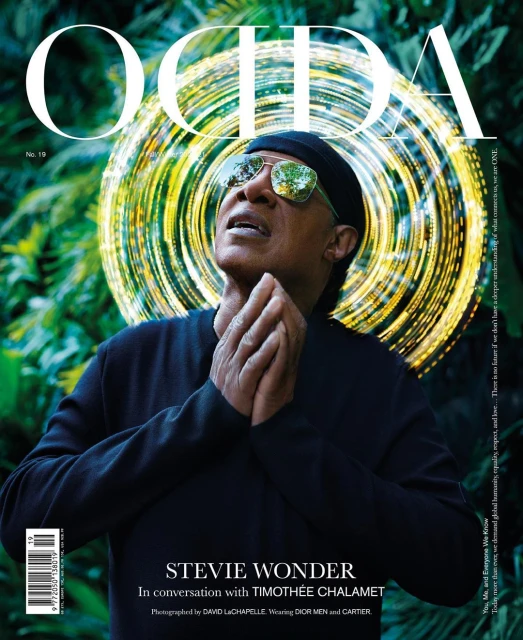 Magazine cover featuring Stevie Wonder wearing sunglasses, a black cap and black sweater, with a green background and radial light effect.