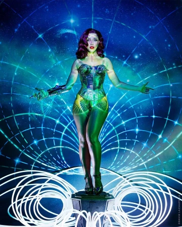 Full shot of a woman with wavy dark hair and green body paint wearing a silver corset and high heels, posing in a digital setting.