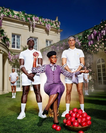 Elegant outdoor fashion shoot features a stylish woman in a purple skirt suit, seated with tennis players and a bowl of red apples.