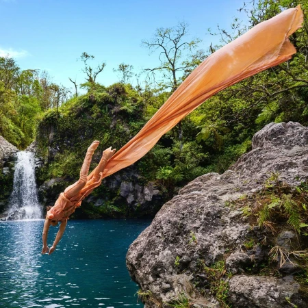 Figure in peach-colored clothing diving into a jungle pool with a waterfall