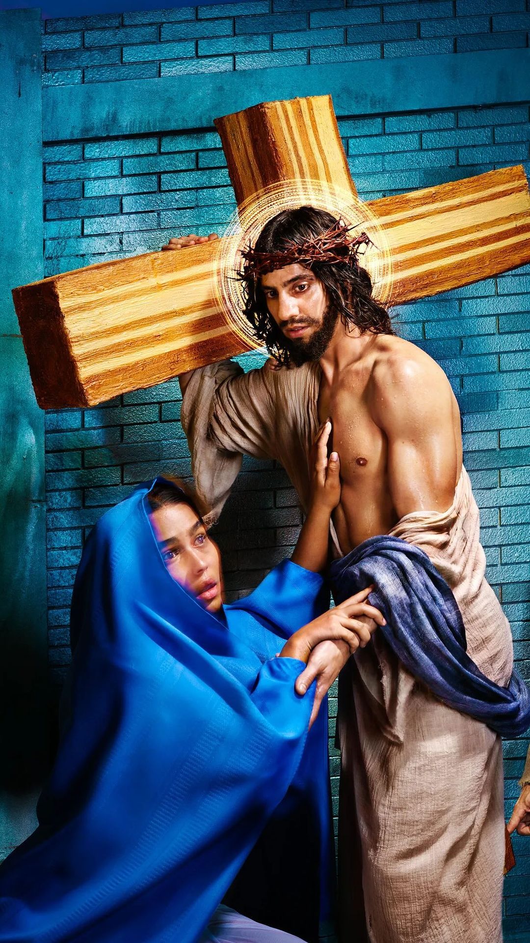 Man with crown of thorns carrying cross, kneeling woman in blue robe. Religious illustration with dramatic lighting, indoor setting.