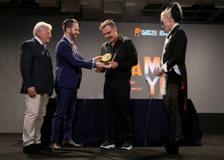 Group of four people onstage at the Florence Biennale Art and Design awards ceremony with a man in a suit presenting an award.