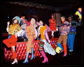 Group of vibrant models posing on a stage with a red tufted banquette by David Lachapelle