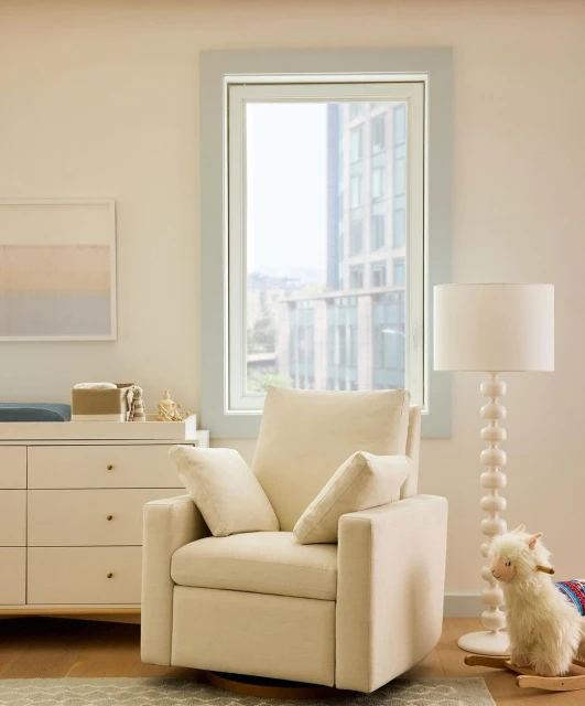 Interior shot of a nursery with a modern armchair, light wood dresser, sheep rocking horse toy, and large window with city view.